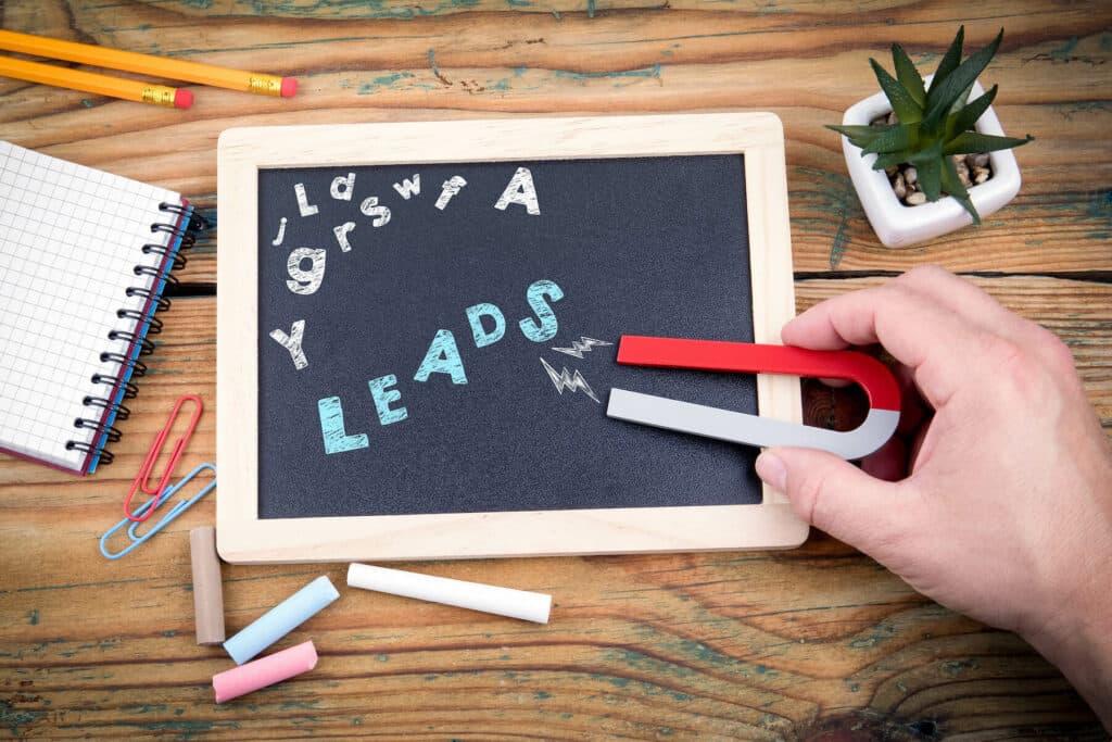 A hand holding a magnet to a small chalkboard with the word "leads" written in blue chalk