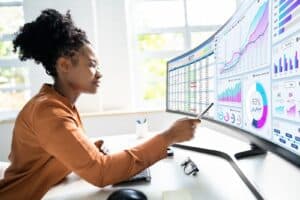 Woman pointing to a monitor with analytics data (Business Intelligence Vs Data Analytics)