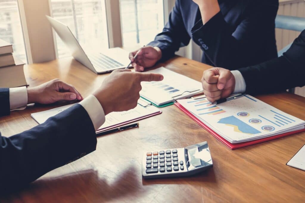 Marketers at a table with papers, a laptop, and a calculator discussing their customer acquisition strategy