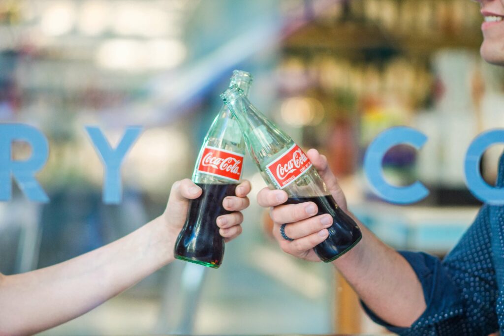 Two people clinking their coke bottles together.