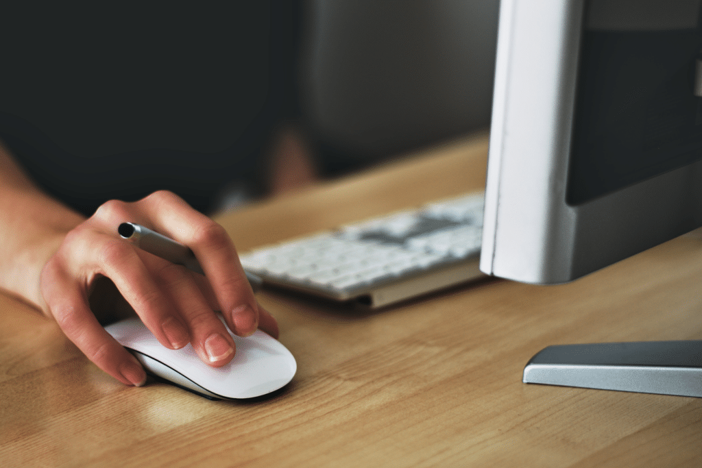 Hand using a mouse next to a desktop computer