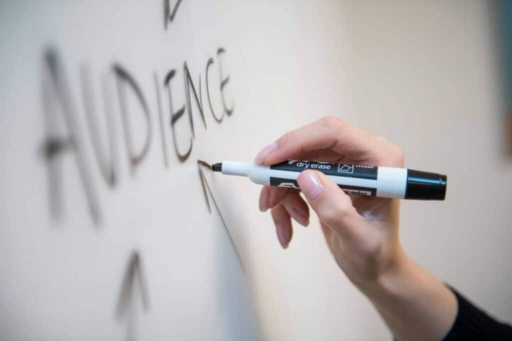 Hand writing the term "audience" on a marker board
