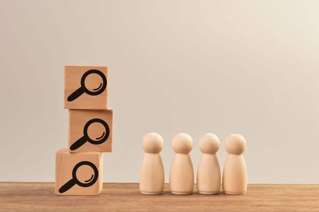Three wooden blocks with magnifying glass emojis drawn on them next to wooden people figurines