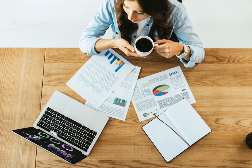Overhead view of a person with coffee looking over documents, a notebook, and an open laptop