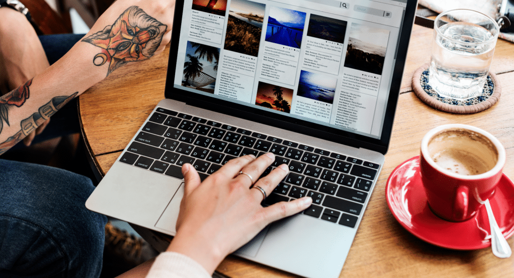 Hand typing on a laptop at a table with coffee and water (content gap analysis)