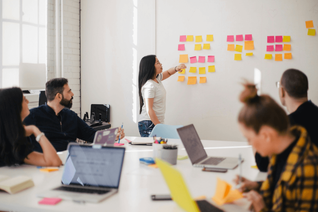 Marketing director in a meeting with other marketing professionals pointing to a wall with sticky notes (website content planning)