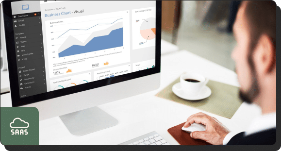A person sitting at a desk using a computer displaying various business charts and graphs on the monitor. A coffee cup and a notebook are on the desk. A "SAAS" label with a cloud icon is at the bottom left corner of the image.